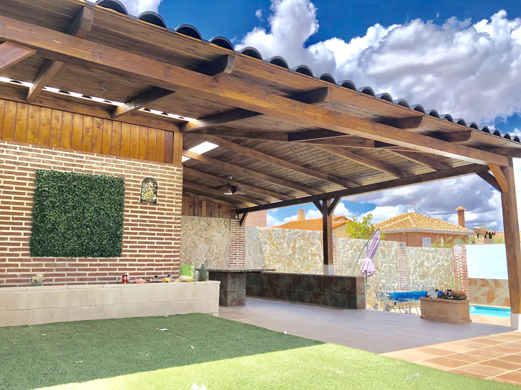 Porche adosado de madera con pilares y cubierta junto a jardín